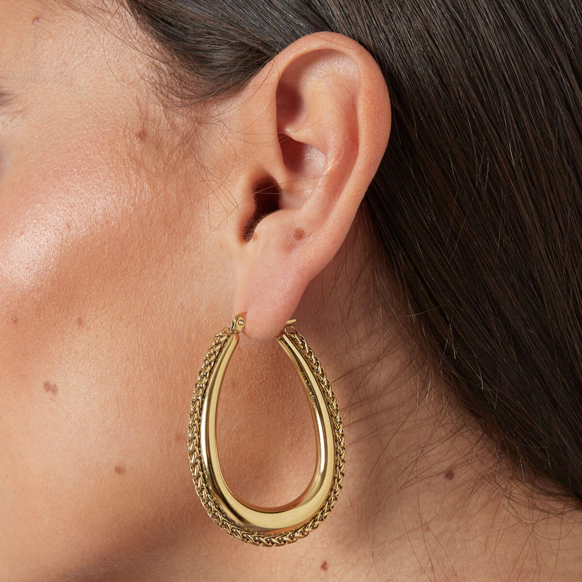 Close up van model met gouden statement oorbellen, gevlochten rand en roestvrij stalen materiaal