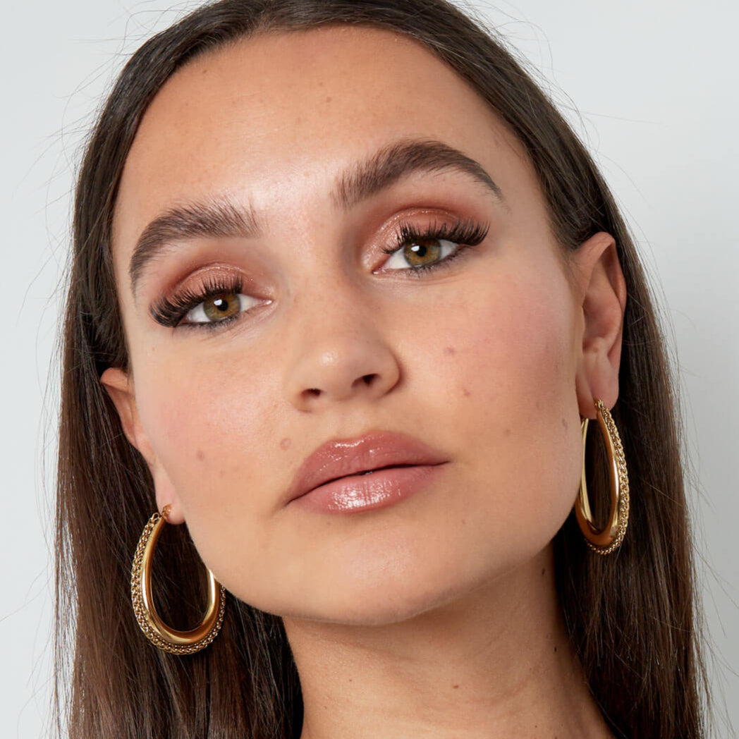 Model draagt gouden statement oorbellen met gevlochten rand, leuke oorbellen dames.
