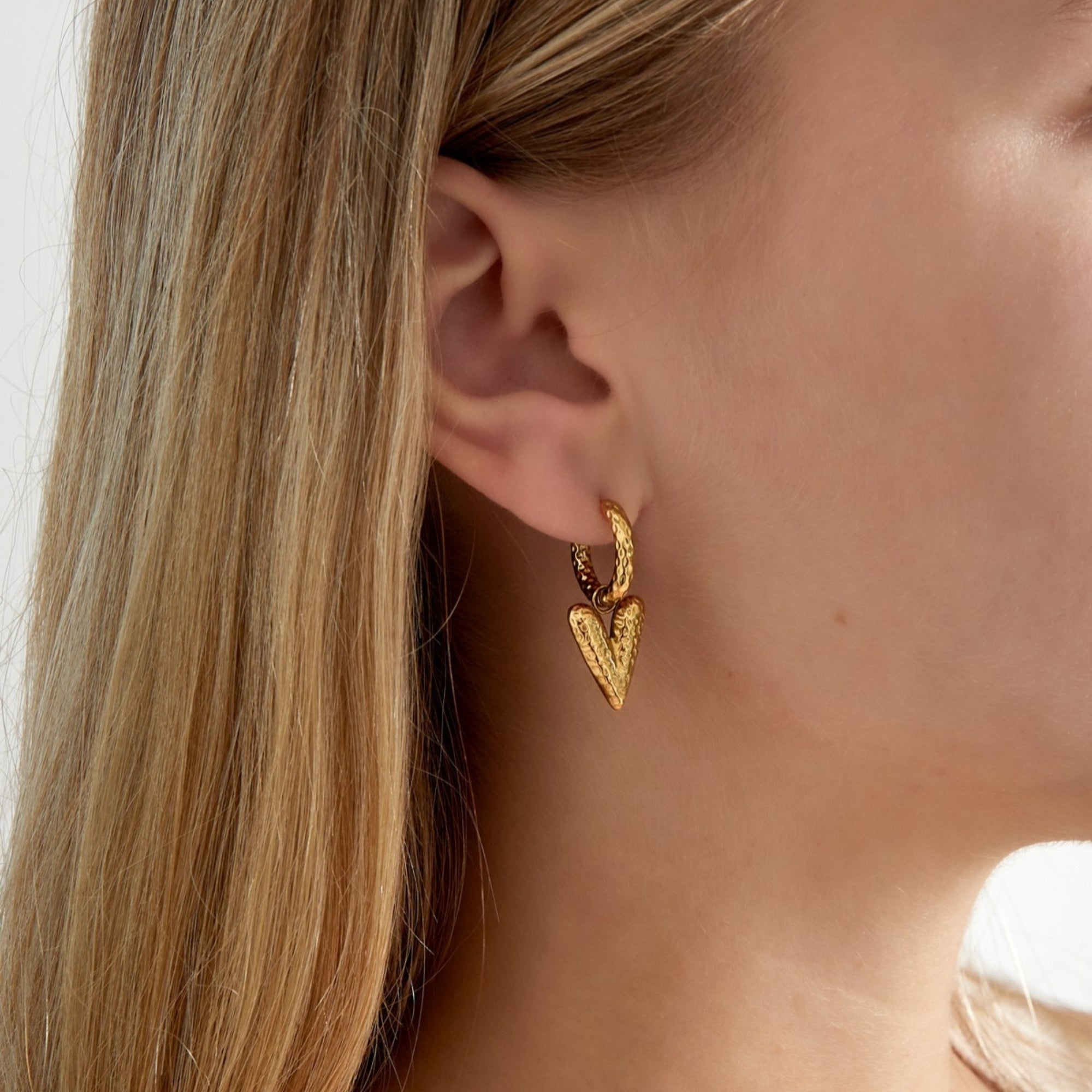 Vrouw draagt goudkleurige hart oorbellen met bubbly structuur, de Hoop You Love Me Bubbly.