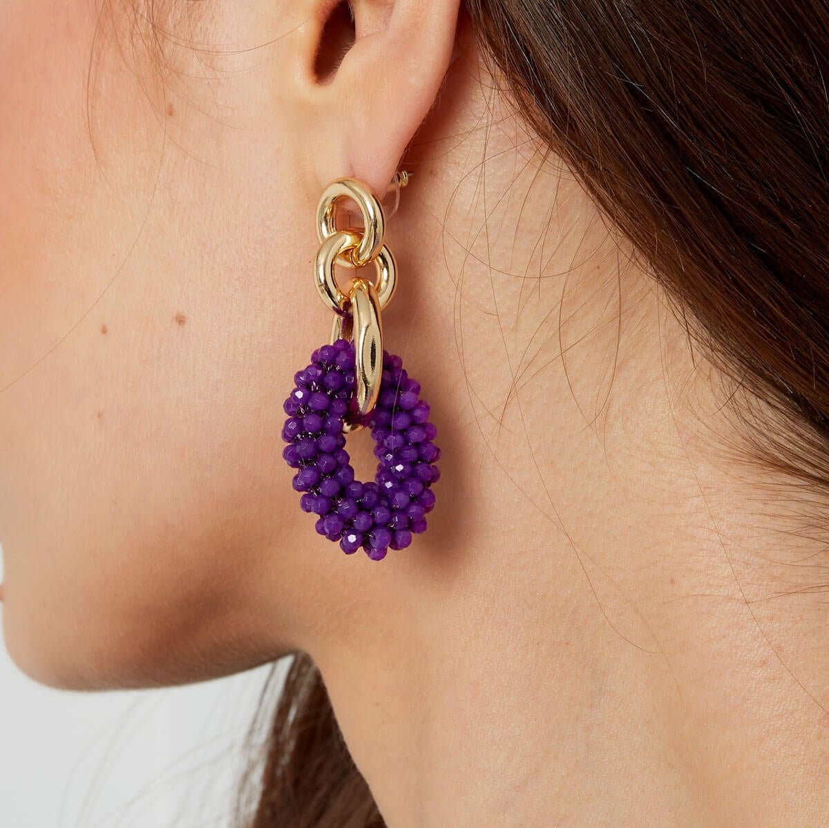 Close up van het model die de schakel kralen oorbellen in het paars draagt de Golden Bond Beads.