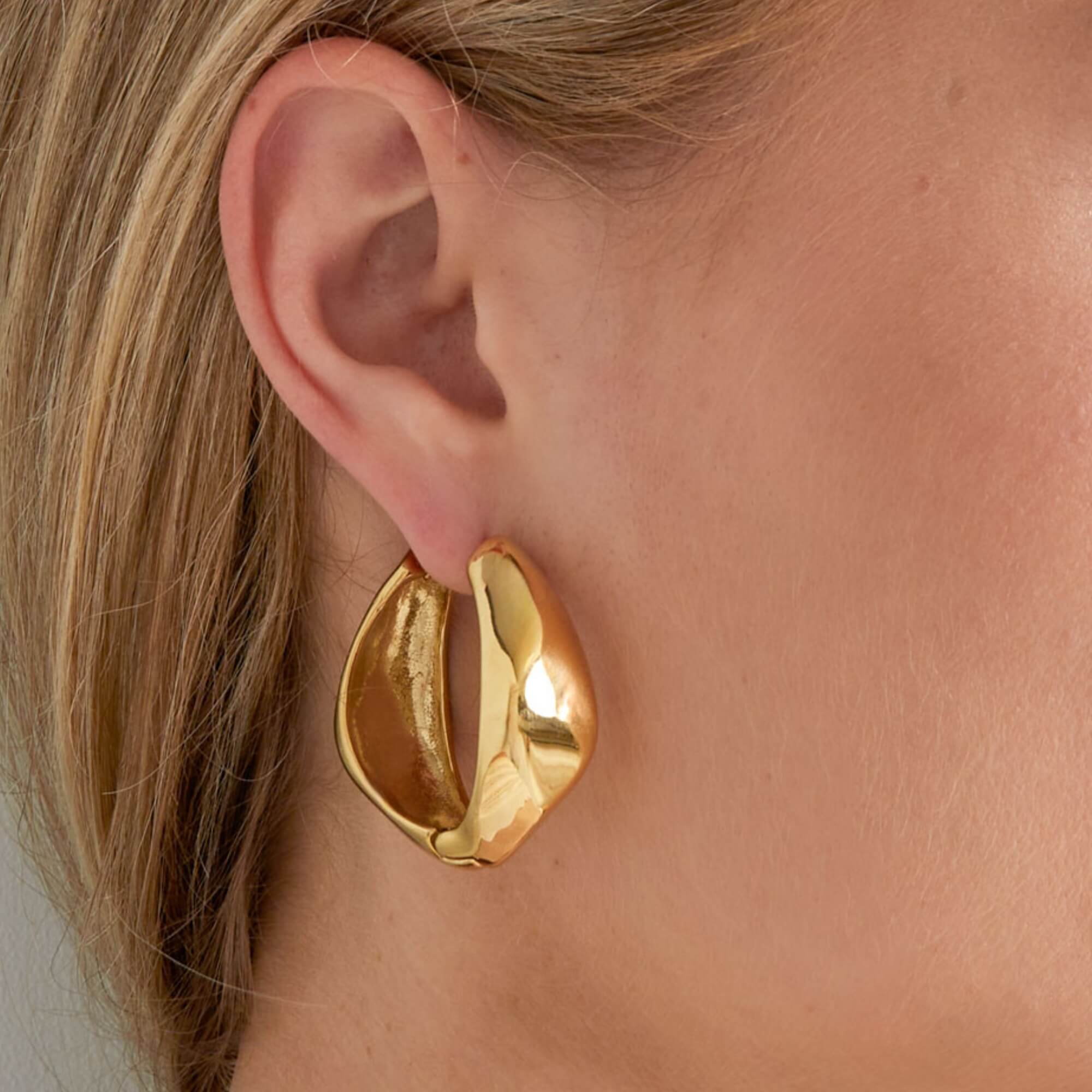 Vrouw draagt goudkleurige Curvy Confidence Hoops oorbellen, nikkelvrije hoops van 3,5 x 3,7 cm.