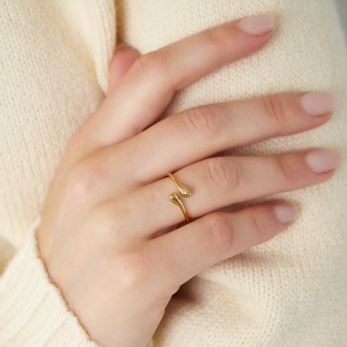 Model draagt een gouden verstelbare ring met een verfijnd open design en druppelvormige details.