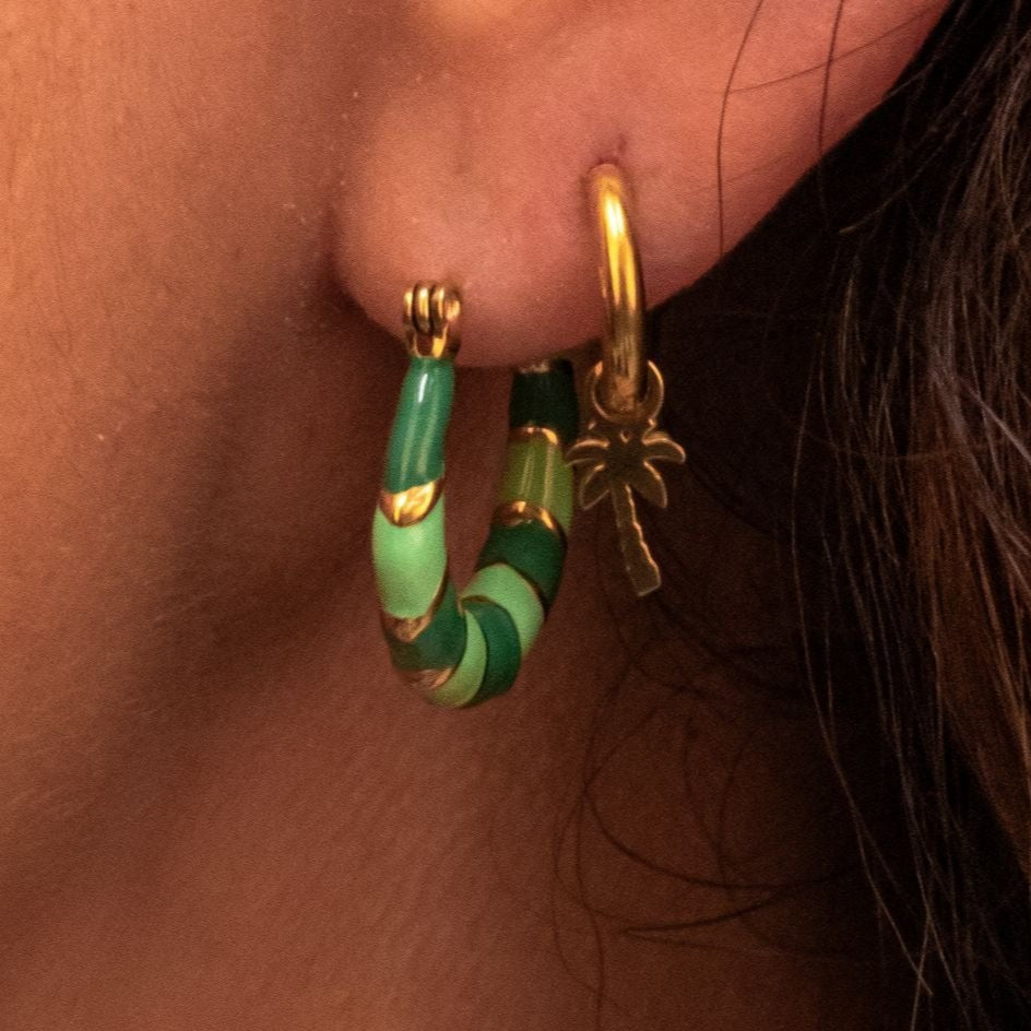 Celia draagt gekleurde creolen in het groen en oorbellen mini palmboom: Model Celia toont onze groene creolen en oorbellen met een mini palmboom bedel, een modieuze combinatie van vrouwen oorbellen.