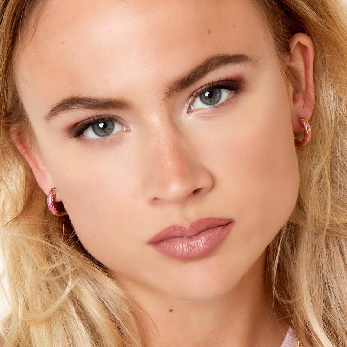 Model draagt Azteca Amor Oorbellen roze – kleurrijke oorringetjes met Azteekse print, perfect voor vrouwen die hun kracht willen uitstralen.