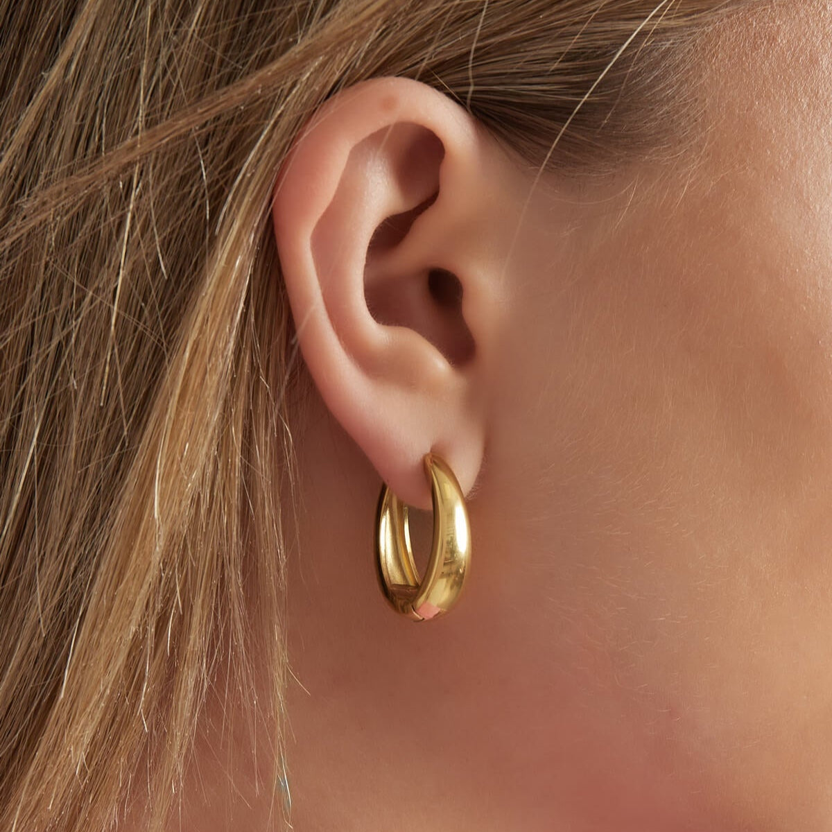 Model draagt goudkleurige Sleek & Chic oorbellen, hypoallergene en simpele oorbellen.