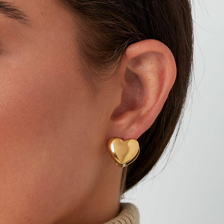 Model draagt gouden hartjes oorbellen, nikkelvrije studs met klapsluiting
