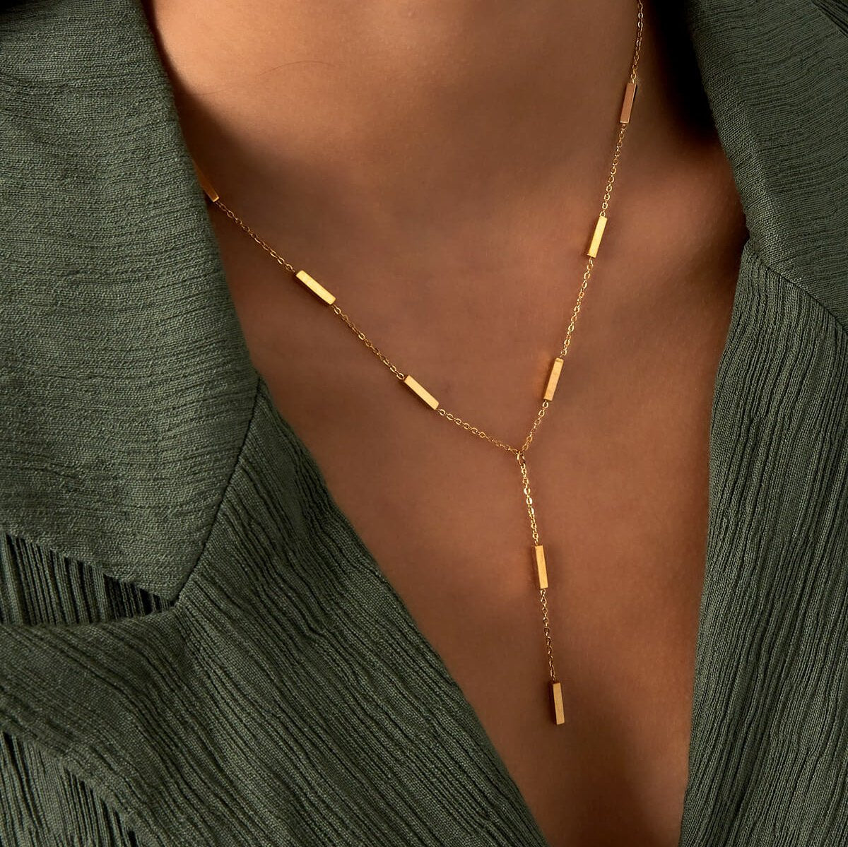 Model draagt een lange gouden ketting met subtiele rechthoekige details – perfect als decolleté ketting voor vrouwen.