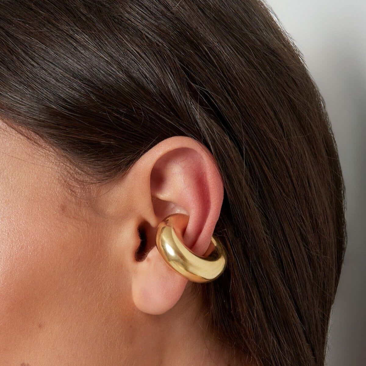 Model draagt een grote gouden ear cuff, een bold en statement accessoire voor een elegante stijl.