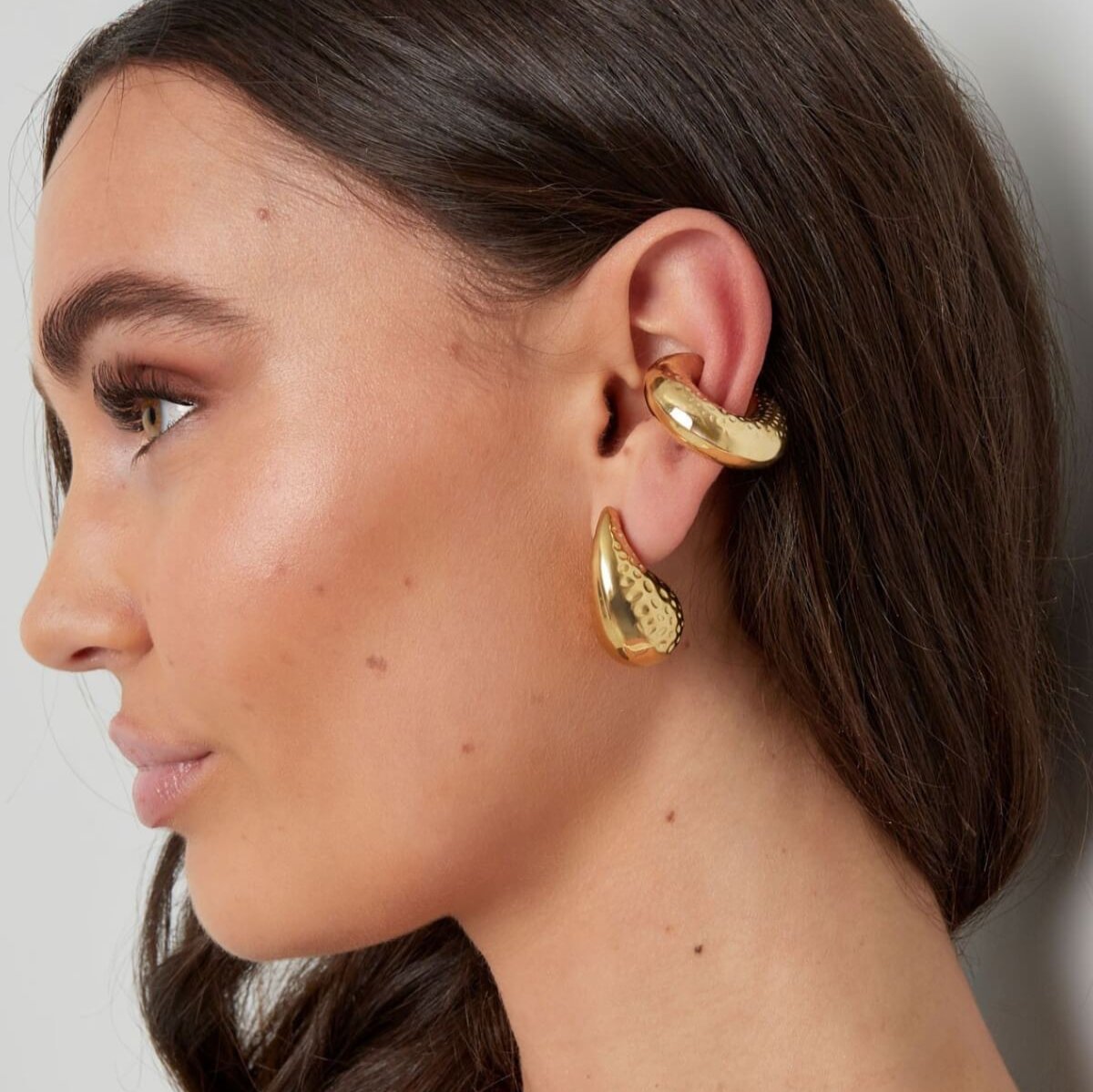 Model draagt een grote gouden bubbly ear cuff, een statement accessoire dat kracht en zelfvertrouwen uitstraalt.