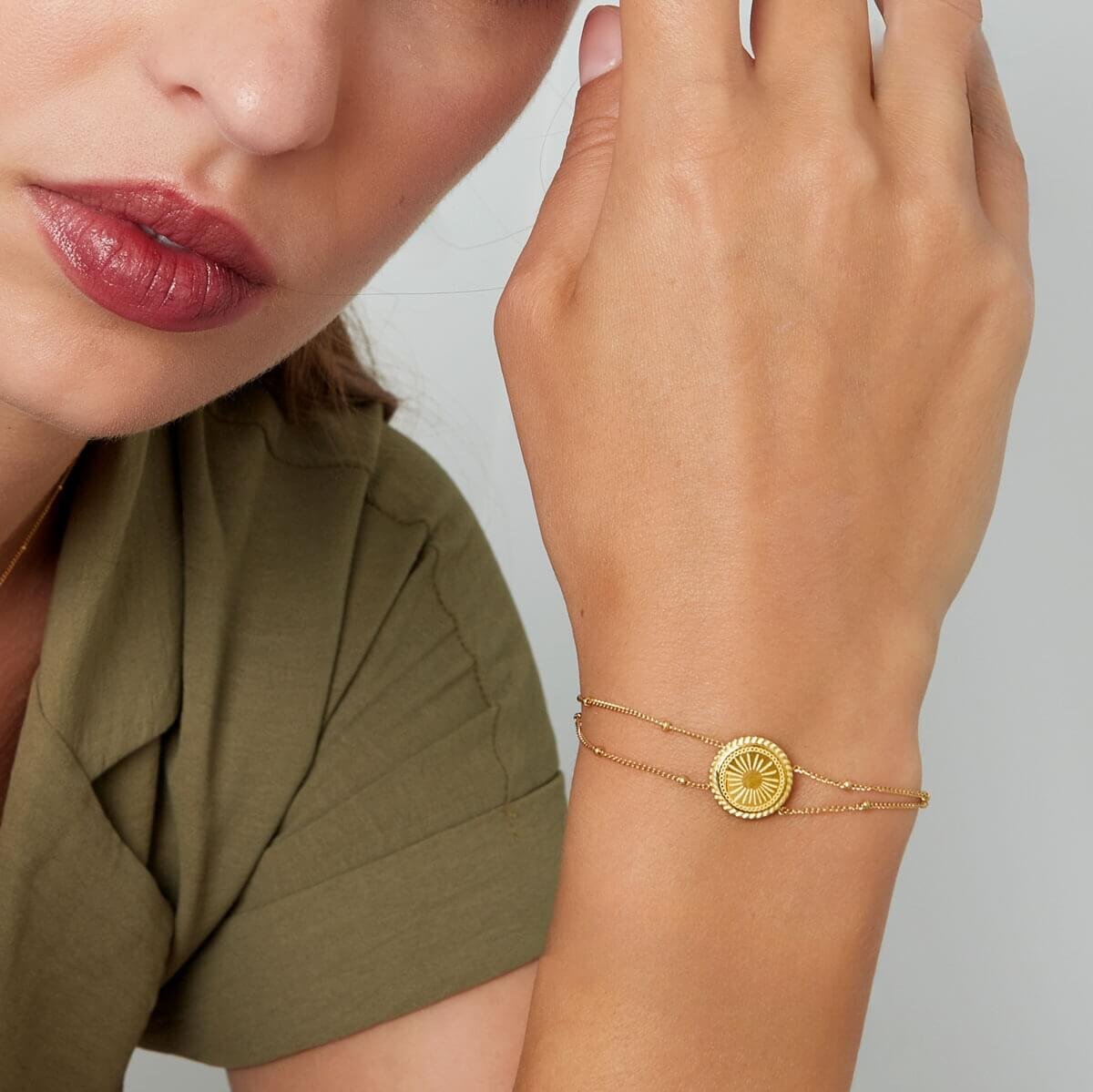 Model met gouden dubbele armband en ronde bedel, een subtiele maar krachtige accessoire voor elke gelegenheid.