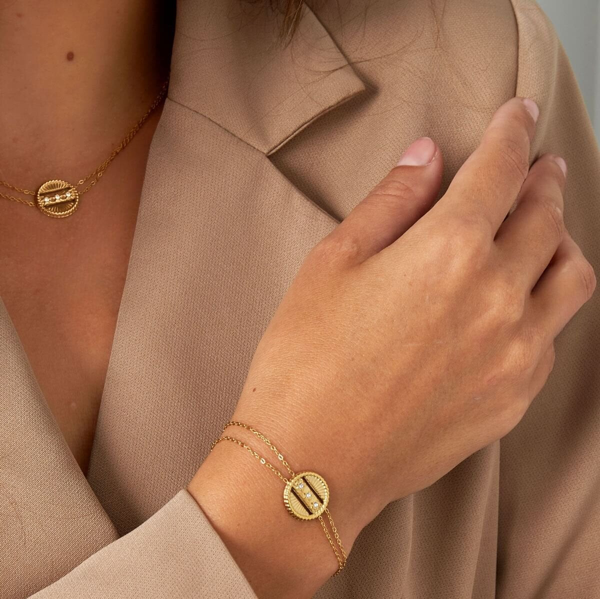 Model draagt de gouden dubbele armband met coin bedel, een subtiele en elegante toevoeging aan elke outfit.