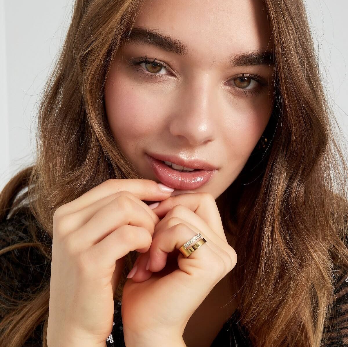 Model draagt een gouden dubbele ring met steentjes, een trendy statement ring.