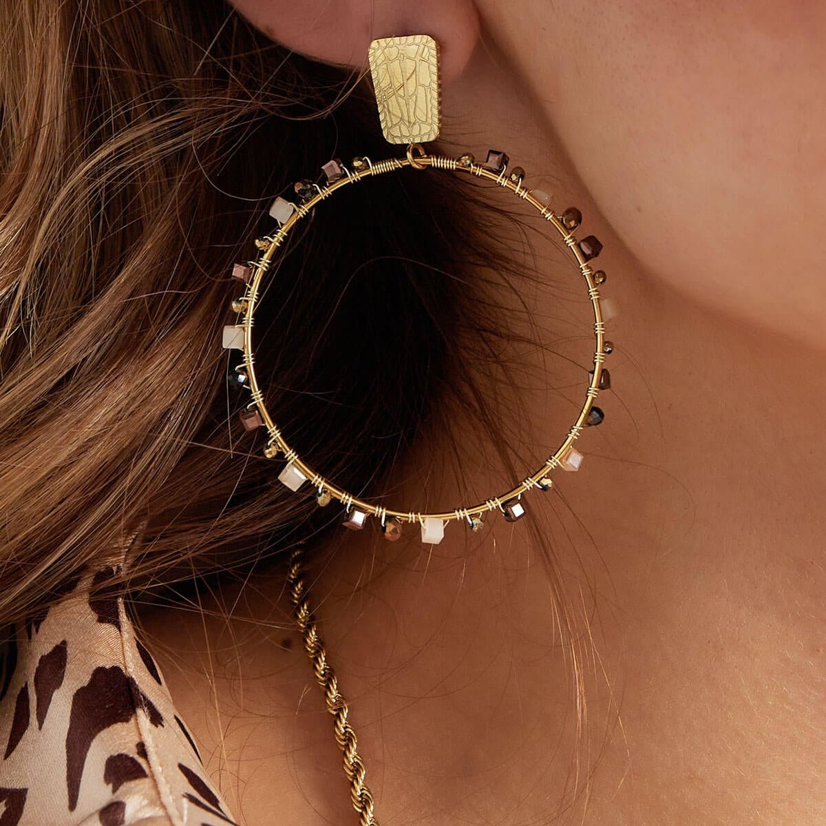 Model draagt gouden hoops met beige kralen, close-up. De hoops zijn gemaakt van roestvrij staal.