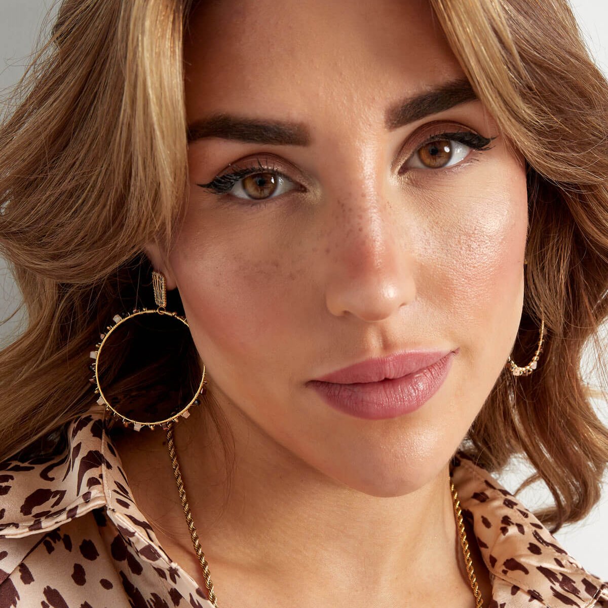 Model draagt gouden hoops met beige kralen, volledige look.